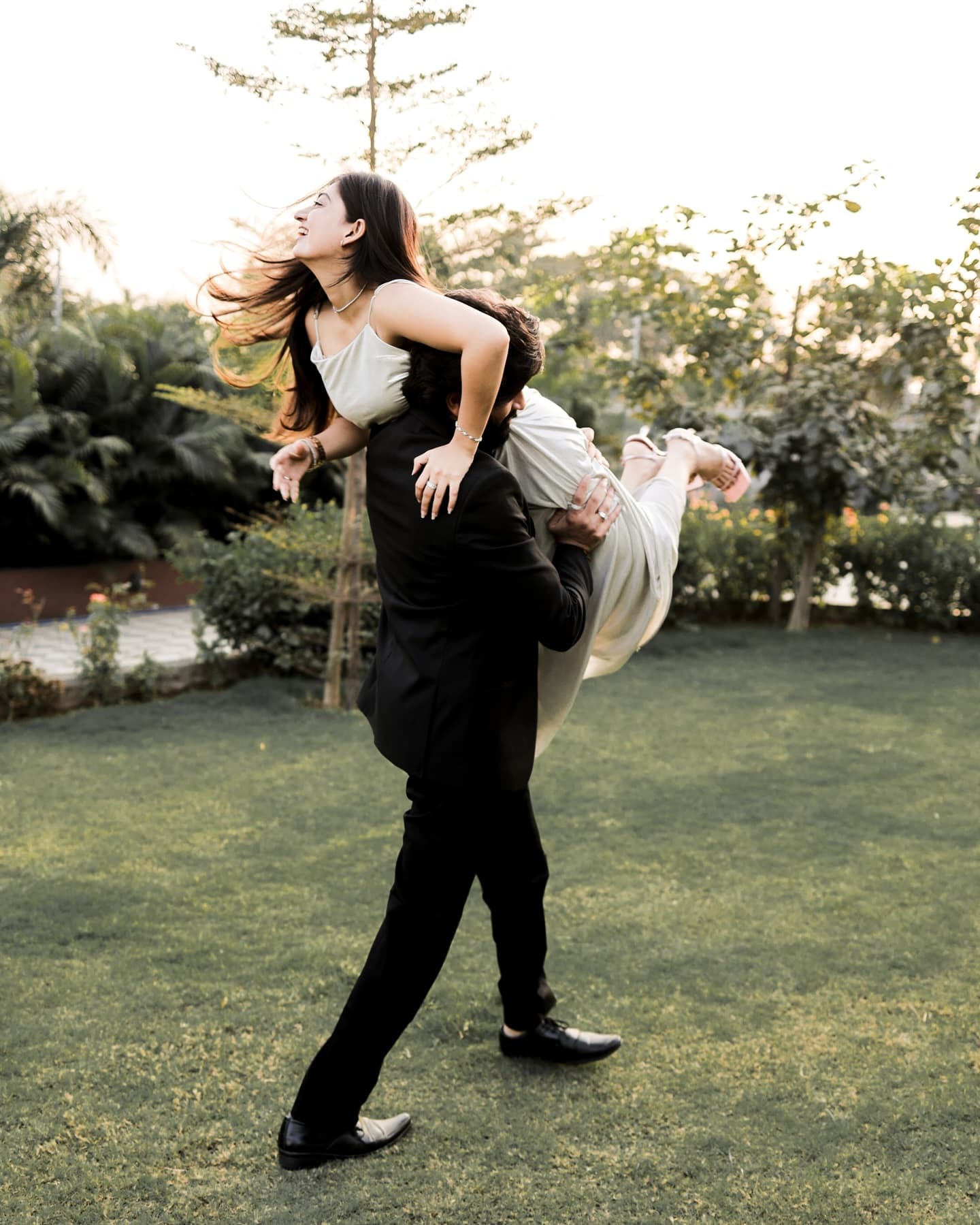 Groom playfully carrying the laughing bride over his shoulder across a garden lawn